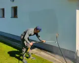 Mężczyzna myje elewację domu myjką ciśnieniową.