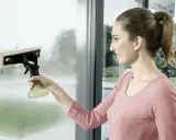 Kobieta z atomizerem i myjką do okien czyści zaparowane okno.