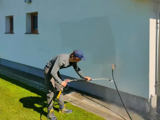 Mężczyzna myje elewację domu myjką ciśnieniową.