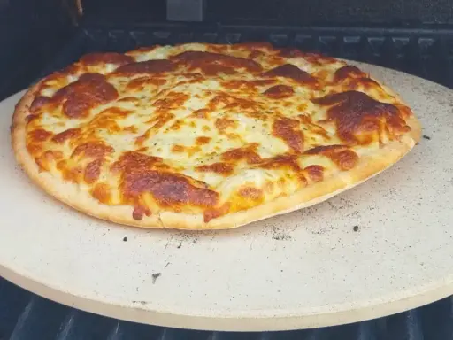 Upieczona pizza z roztopionym serem na kamieniu do pizzy na grillu.