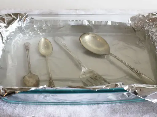 Srebrne sztućce w szklanej misce wyłożonej folią aluminiową.