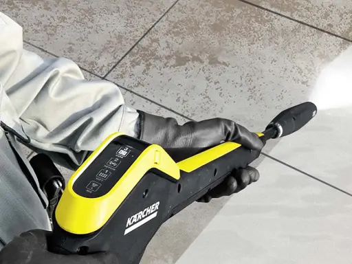Dłoń w rękawicy trzyma myjkę ciśnieniową Karcher, która myje brudne płytki.