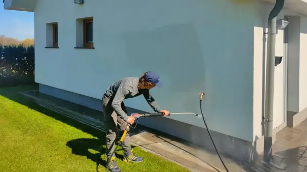 Mężczyzna myje elewację domu myjką ciśnieniową.